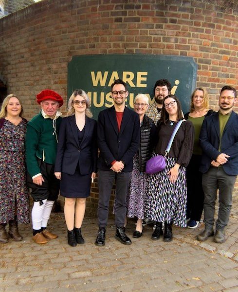 Nine people gathered outside Ware Museum to celebrate its 40th anniversary, with local MP Josh Dean standing in the centre of the group. One person is dressed in historical costume, and the Museum’s sign is visible behind them.
