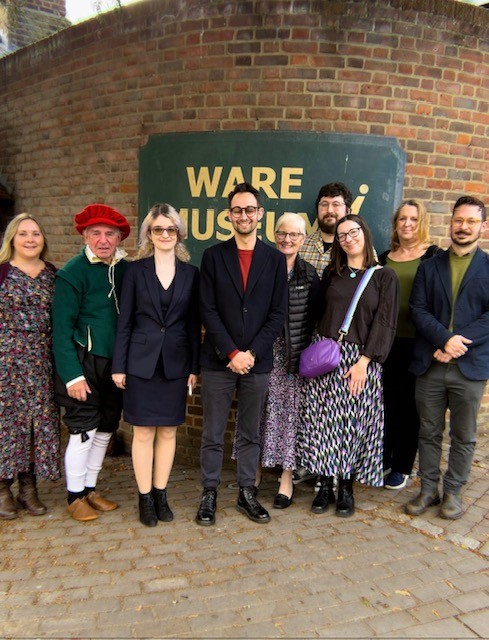 Nine people gathered outside Ware Museum to celebrate its 40th anniversary, with local MP Josh Dean standing in the centre of the group. One person is dressed in historical costume, and the Museum’s sign is visible behind them.